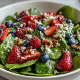 Freshly tossed Spinach and Berry Salad Bowl featuring toasted walnuts, sliced red onion, and a drizzled balsamic vinaigrette on a white plate.