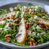 Arugula and Pear Bowl salad with glistening balsamic vinaigrette, juicy pear wedges, blue cheese crumbles, and chopped pecans, ready to serve as a light main course.