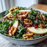 A close-up of the Kale and Pomegranate Bowl drizzled with honey-Dijon dressing, highlighting the ruby seeds, green leaves, and toasted nuts for a healthy salad.