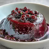A single Black Currant Panna Cotta ramekin garnished with fresh berries and mint.
