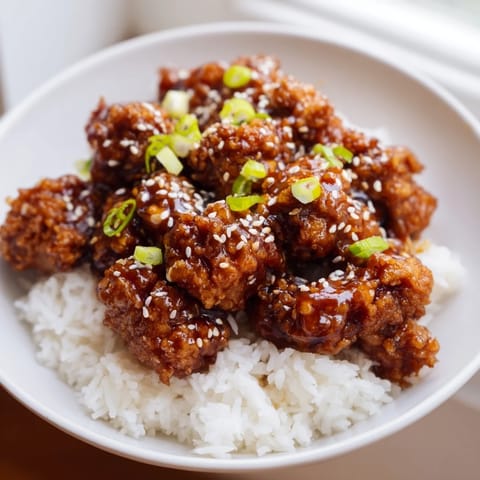 Steaming white rice is pictured under a generous portion of flavorful General Tso's Chicken.