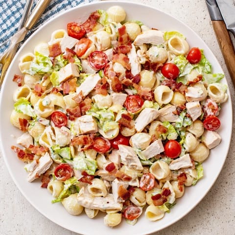A close-up of BLT Chicken Pasta Salad, featuring creamy dressing, crisp romaine, juicy cherry tomatoes, and tender grilled chicken in pasta shells.  