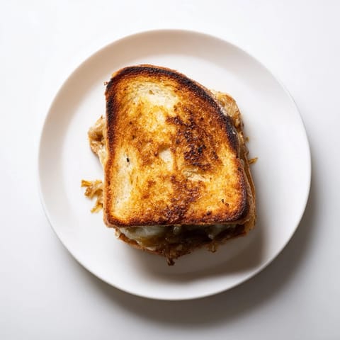 A close-up view of a toasted Caramelized Onion & Gruyère Grilled Cheese sandwich, melted cheese stretching between buttery, golden-brown bread slices.
