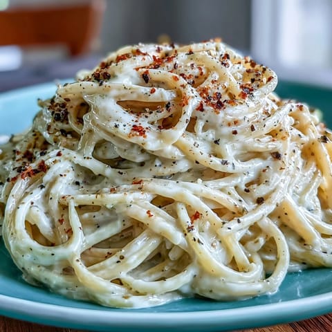 A skillet of Cacio e Pepe, with steam rising and Pecorino Romano melted into a glossy, peppery coating.