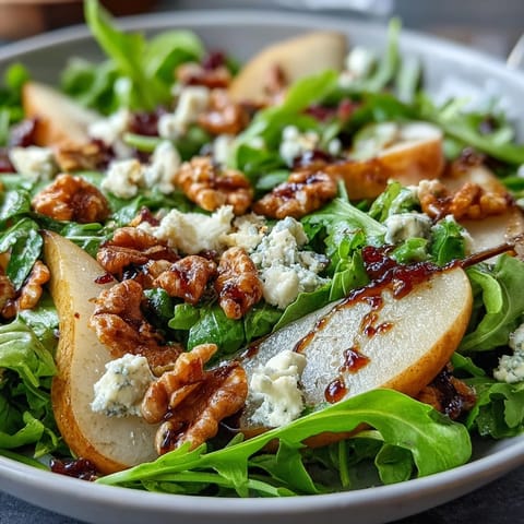 Freshly tossed Arugula and Pear Bowl featuring peppery greens, sweet ripe pear slices, creamy crumbled cheese, and crunchy toasted walnuts on a rustic wooden table.