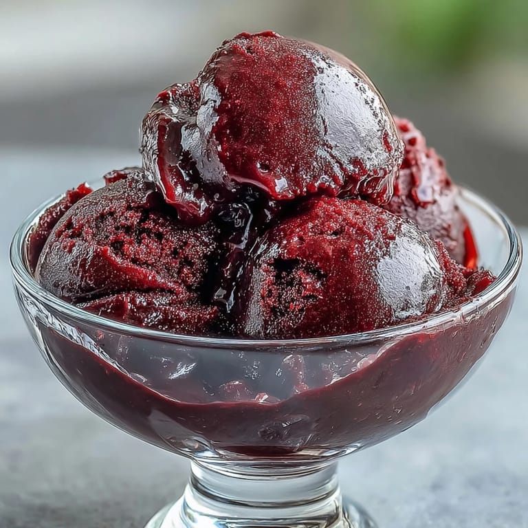 Smooth and refreshing black currant sorbet in a glass dish, topped with lemon zest and a sprig of mint for a pop of color.